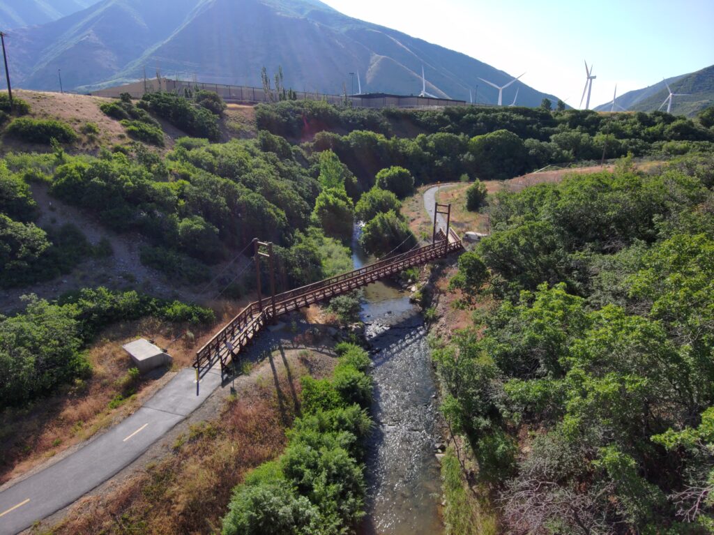 A flat paved trail with tree shade running along a river
