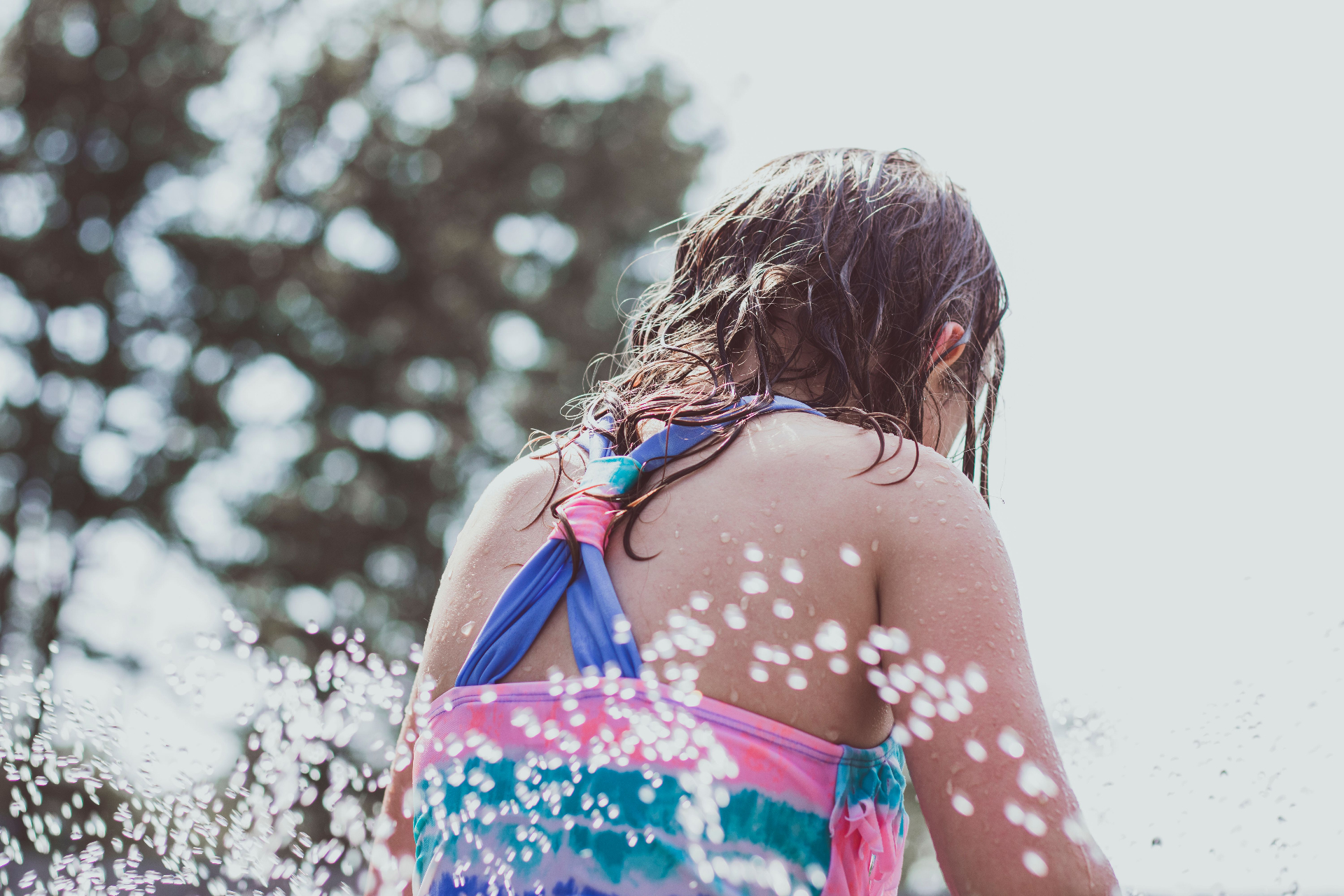 A child in a swimsuit playing in splashes of water on a sunny day