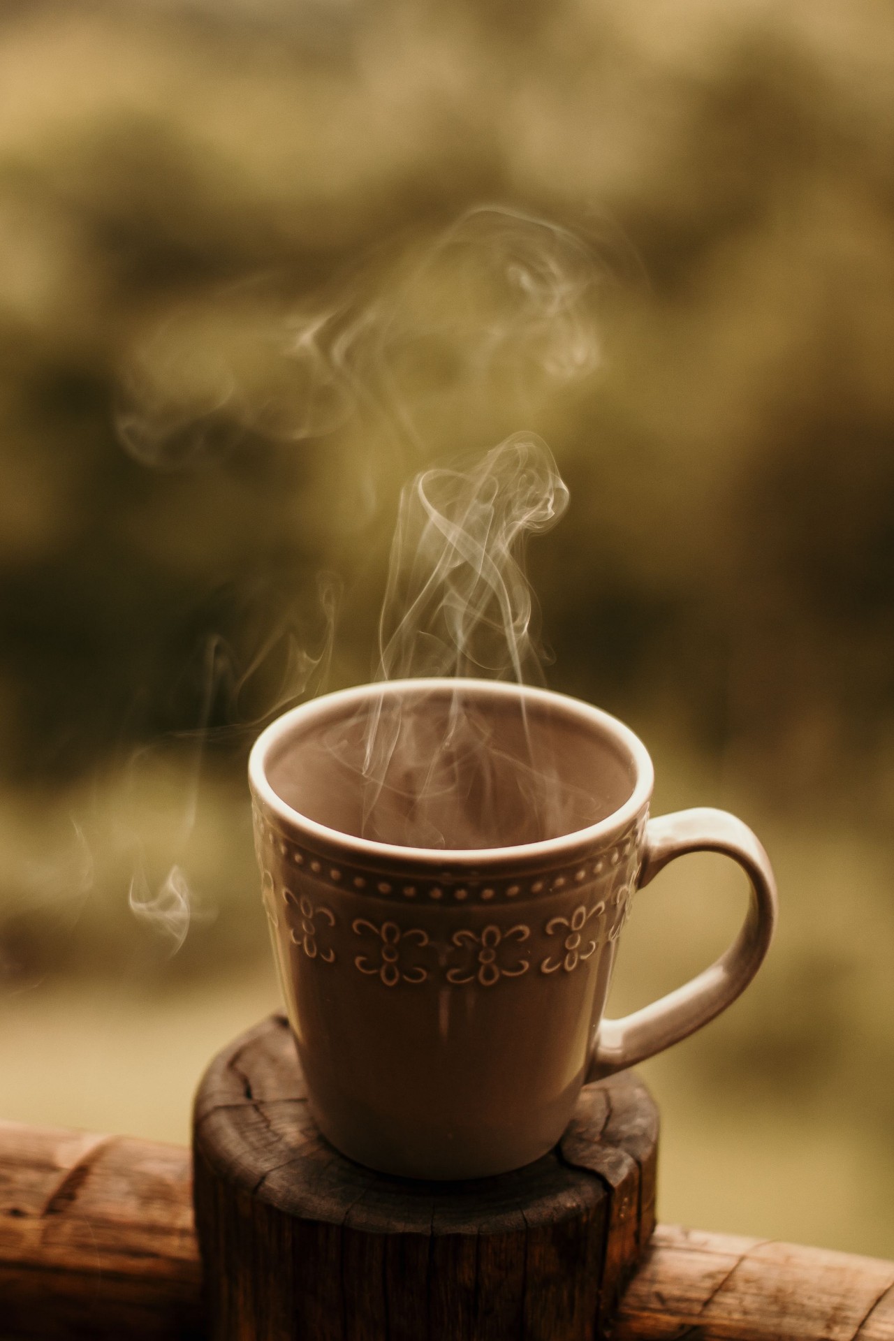 Steaming coffee cup on a wooden post outdoors