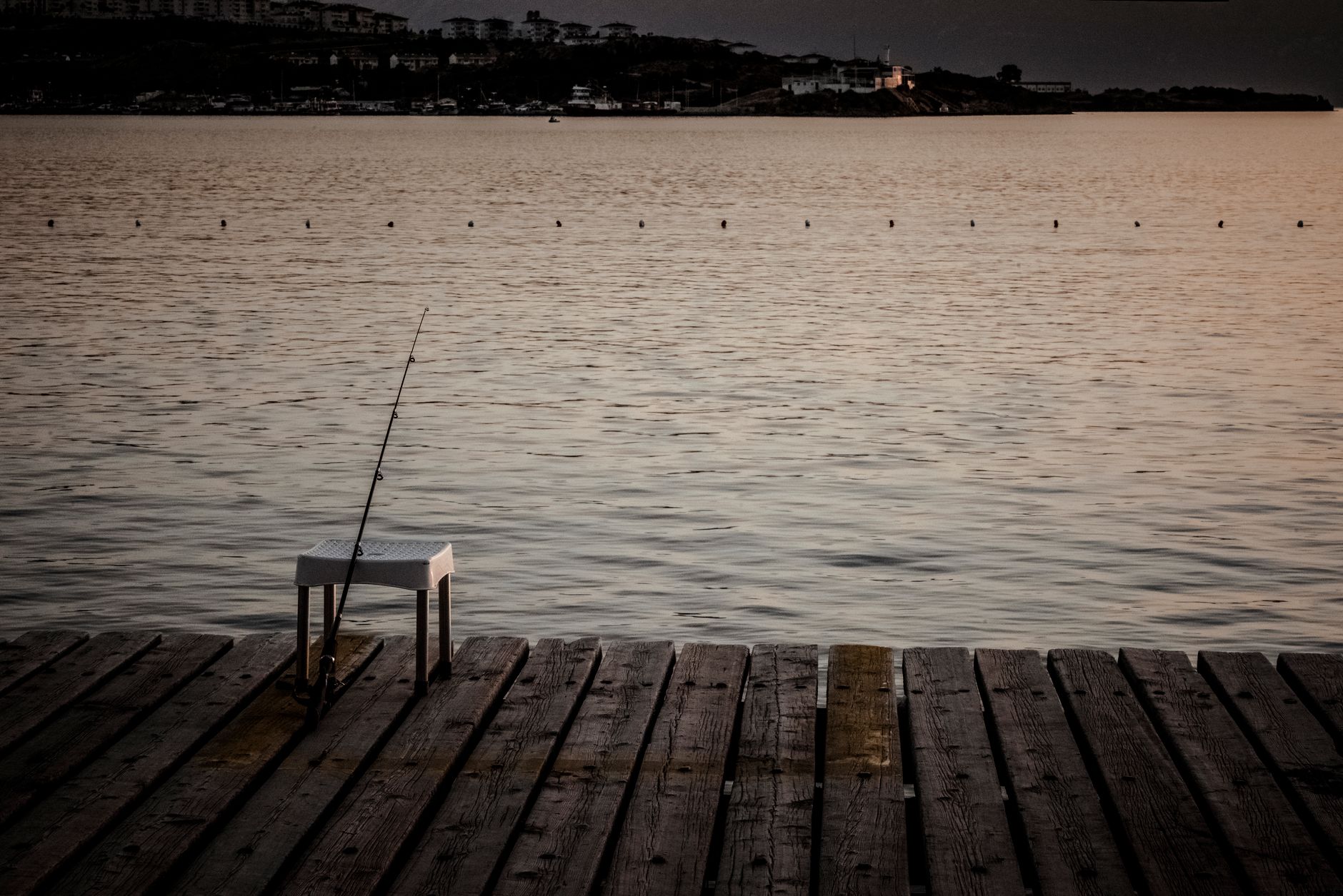 A fishing rod set up on a lakeside pier at twilight